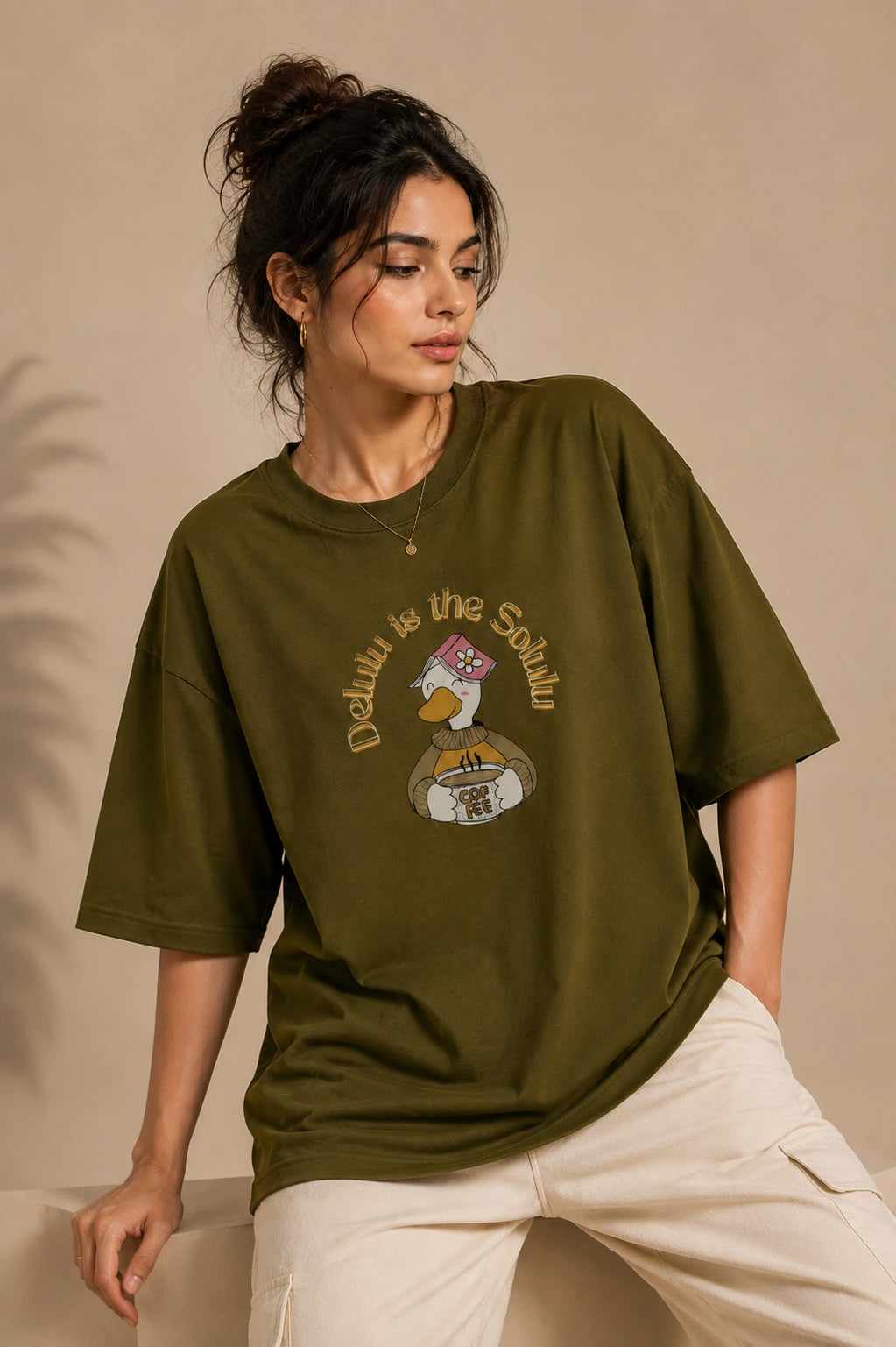 Female model wearing Delulu Is The Solulu olive green unisex graphic streetwear T-shirt made from premium 240 GSM cotton