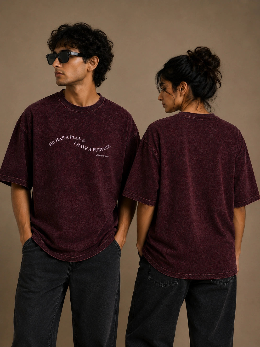 A man and a woman modeling a washed dark burgundy t-shirt, showing both the front and back views. The front features white text that reads 'HE HAS A PLAN.