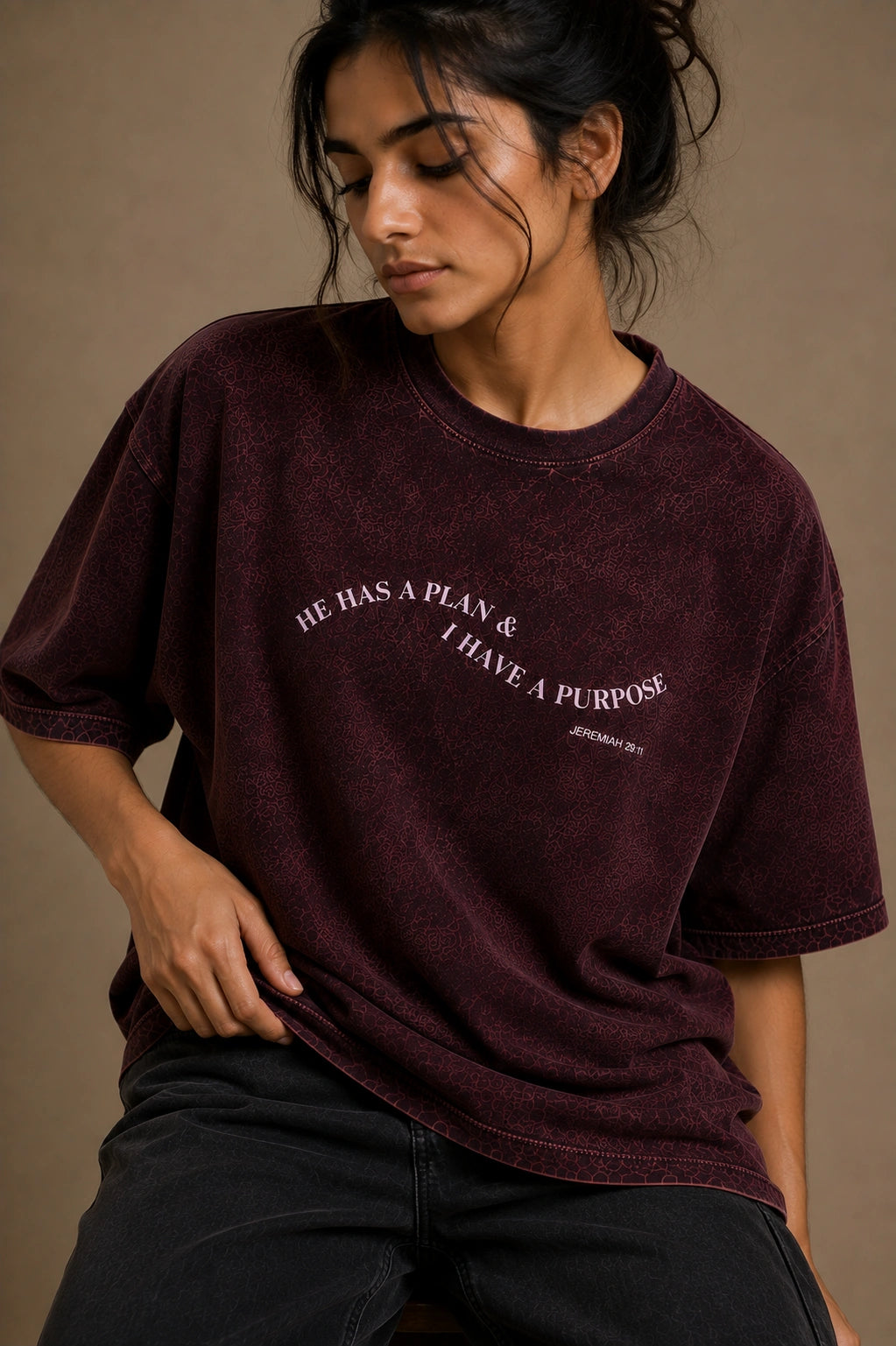 A woman wearing an oversized maroon mineral-wash t-shirt with the text 'HE HAS A PLAN.